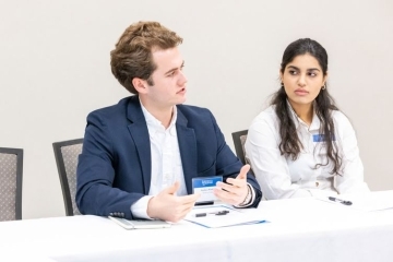 two students discuss at a roundtable while wearing business attire