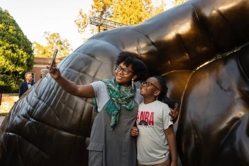 two young people smile and take a selfie in front of a sculpture