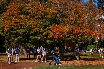Students wearing backpacks walk past bright autumn foliage on the chambers lawn