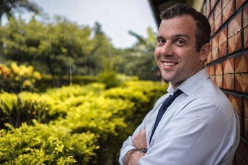 a man in a doctor's jacket smiles leaning against a brick wall