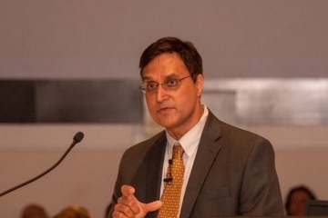 a man wearing a suit and tie speaks into a microphone on stage