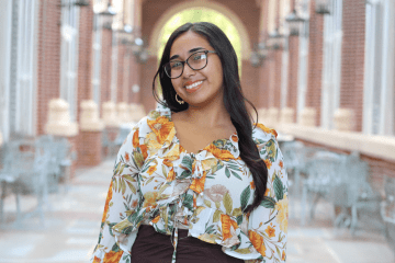Headshot of young female student on campus, with long dark hair and glasses