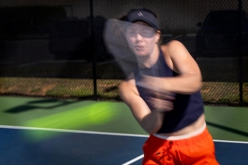 a young woman swings at a pickleball on a court