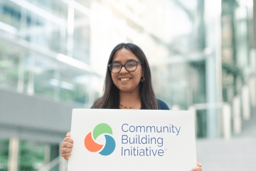 a young woman holds a sign that says "community building initiative"
