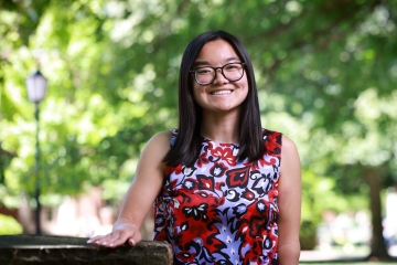 A smiling student with glasses and straight, dark hair poses outside wearing a sleeveless floral patterned blouse.