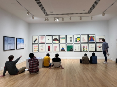 Students sitting at a gallery exhibition with art on the wall