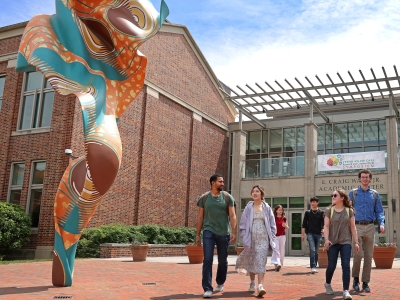 a group of students walk out of an academic building on a college campus on a sunny day
