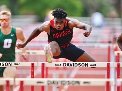a young Black man hurdles on a track wearing a Davidson College uniform
