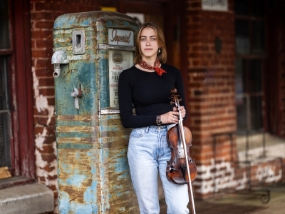 a young white woman holding a fiddle in an old gas station