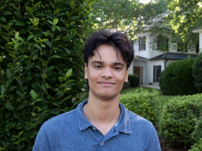 a young man with dark hair wearing a blue collared shirt on a sunny morning