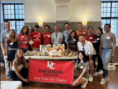 Group of alums in t-shirts holding a Davidson College pennant flag with the words "New York City Chapter" below the primary lockup