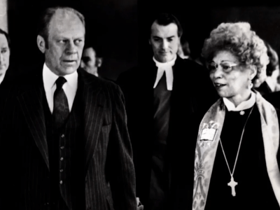 a Black woman walks and talks with an older white man in a black and white photograph