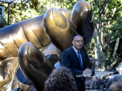 Anthony Foxx addresses the crowd at the podium in front of the hands sculpture
