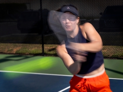 a young woman swings at a pickleball on a court