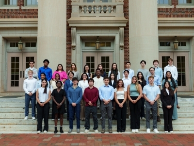 a group of students in business attire stand in front of a brick academic building