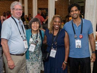 Four attendees pose closely together smiling, each wearing lanyard name tags reading "Reunion '26".