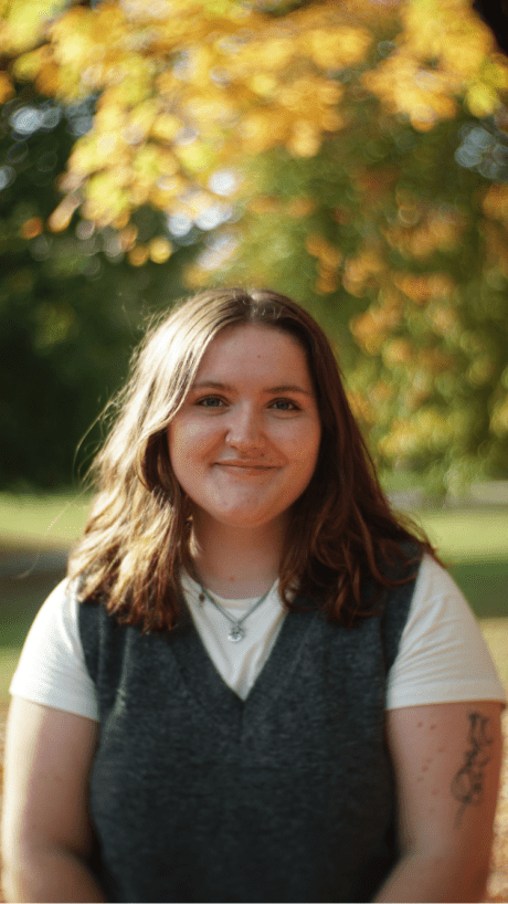 a young white woman wearing a tshirt and sweater vest outside