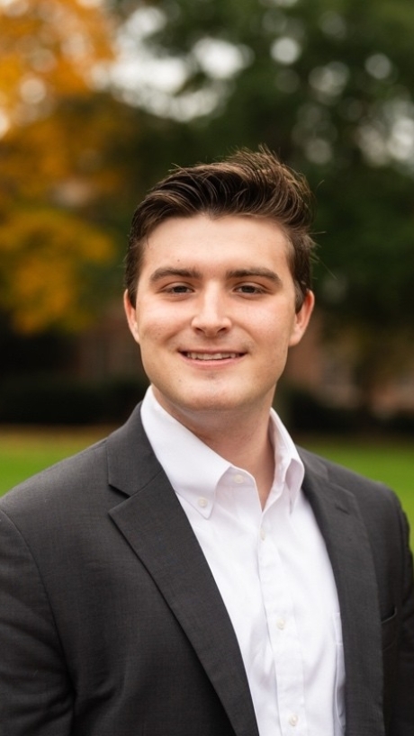 a young white man wearing a white collared shirt with a black jacket while standing outside
