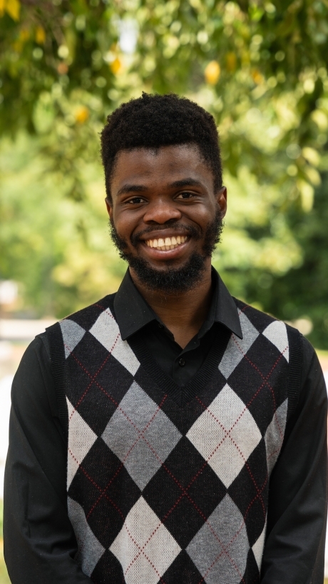 a young Black man wearing a black and grey sweater vest and smiling
