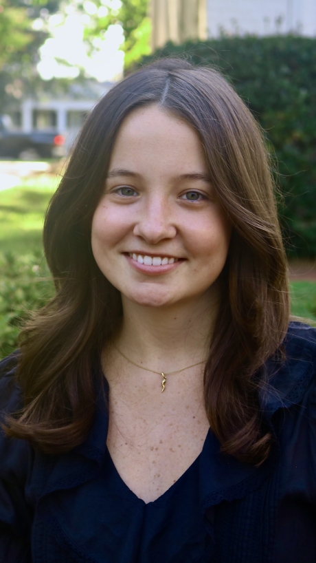 Annalee smiling outdoors with shoulder-length wavy dark hair and a black top.