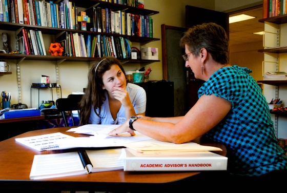 Prof. Molinek sits in her office with student looking at printed materials
