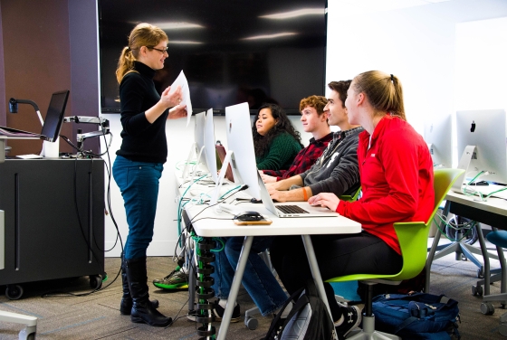 Prof. Peck talks to four students that each use a desktop computer