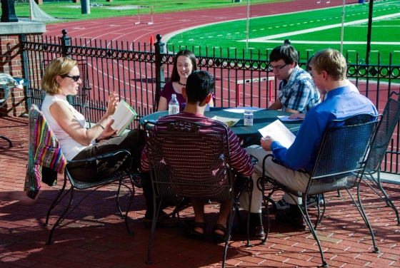 Prof. Neumann leads class at an outdoor table with the track and football field in the background