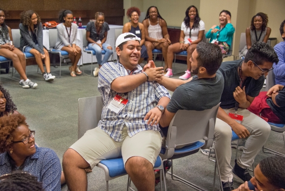 Two students sit next to each other during a team building game surrounded by other students