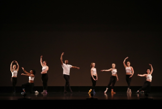 Dancers on stage take different positions in front of a black background
