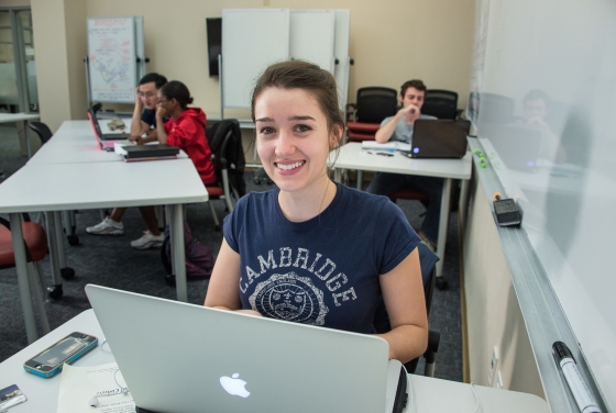 Student smiles at camera with tutoring supplies in front of her and people being tutored in the background