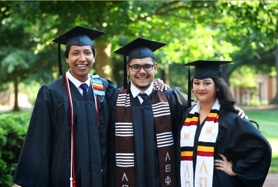 three students standing and smiling in graduation robes