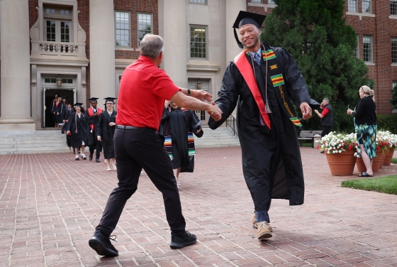 A man shakes hands with a student in graduation robes