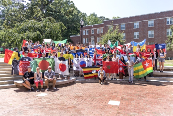 A large group of students in front of a brick building holding flags from around the world