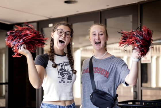 two young women hold pom poms and smile while cheering