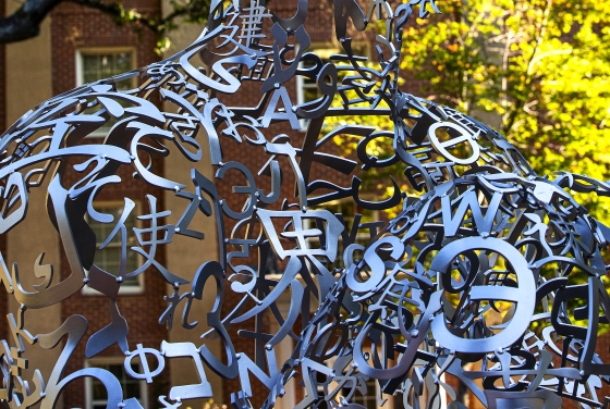 a silver sculpture made of metal letters with yellow and green foliage in the background