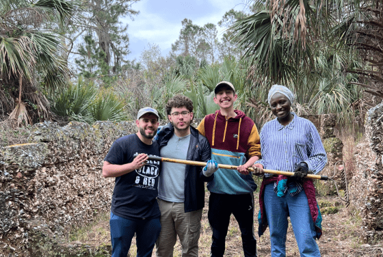 a group of four young people hold a wooden tool in a tropical scene