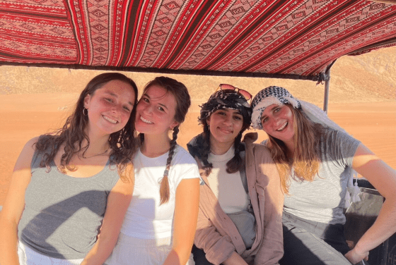 a group of four young women smiling together in a desert environment