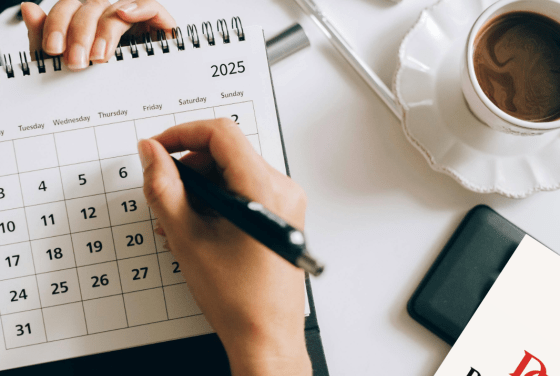a hand writes on a calendar with a coffee next to it