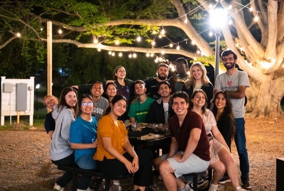a group of young people sitting together at night with string lights in the background