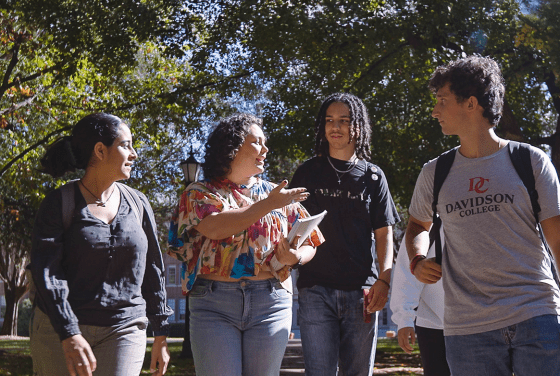 a group of four students smile and walk together while talking on a sunny day