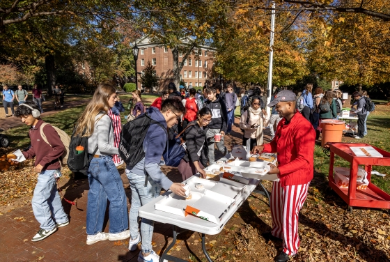 Beautiful fall campus scene with lots of students and a chaplain dressed in striped pants, handing out donuts