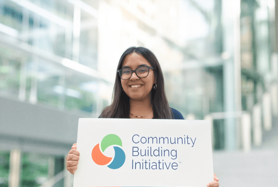 a young woman holds a sign that says "community building initiative"