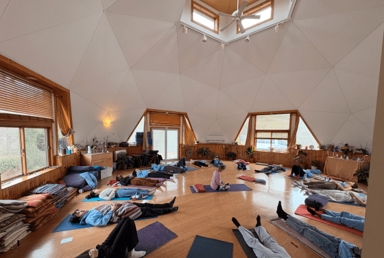 A group of students laying horizontally on yoga mats in a geometric, yurt-shaped space