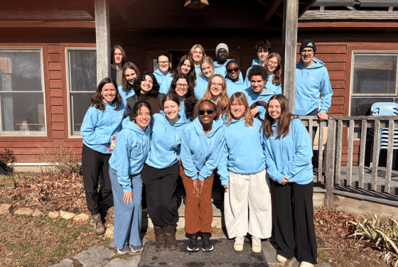 A group of ~20 students and trip ambassadors in blue sweatshirts outside of a mountain cabin