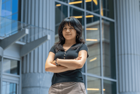A female student stands with arms crossed, wearing a blue polo and khakis