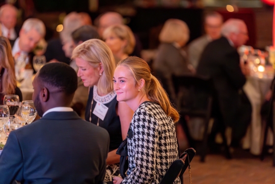 a young woman smiles at a speaker while seated at a dinner