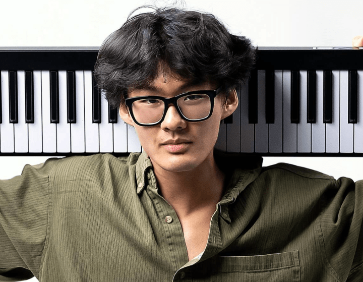 a young Asian man holding a keyboard on his back while sitting cross-legged