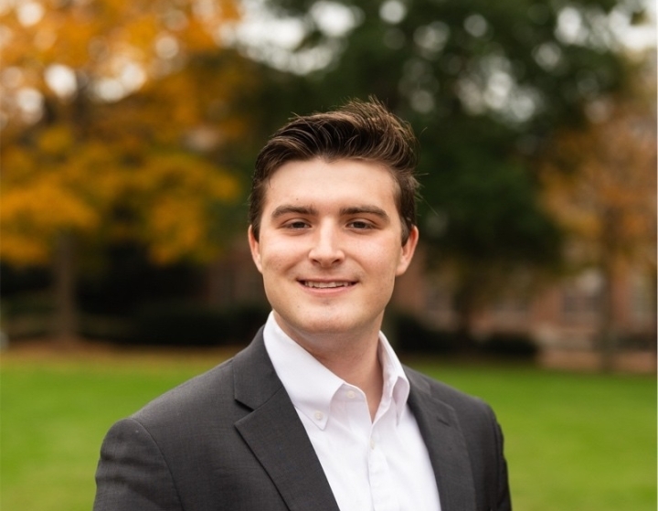 a young white man wearing a white collared shirt with a black jacket while standing outside