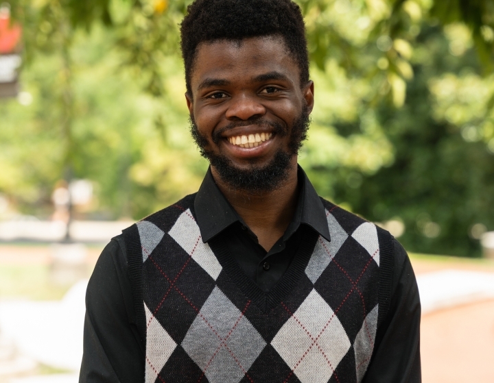 a young Black man wearing a black and grey sweater vest and smiling