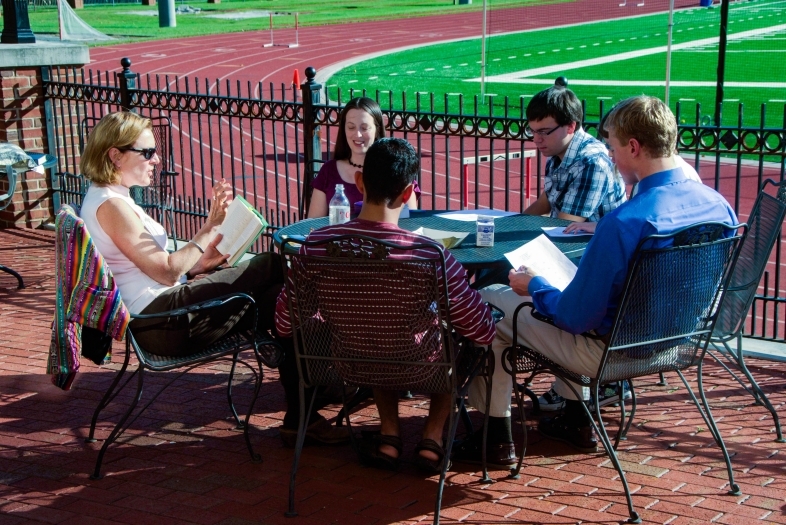 Prof. Neumann leads class at an outdoor table with the track and football field in the background